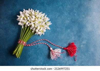A bouquet of snowdrops flowers and a red and white rope with tassels, a symbol of the arrival of spring on a blue background. Postcard for the feast of March 1 Martisor and Baba Marta, space for text.