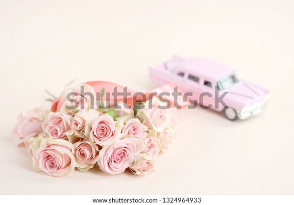A bouquet of spray roses and a pink toy car.\
Free space to place text. Light background. The concept of holiday\
greetings.