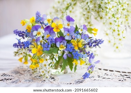 A bouquet of spring blue, yellow flowers in a vase on the table. Pansies, forget-me-nots, primroses, bird cherry, violets, muscari. Postcard, blur, selective focus.