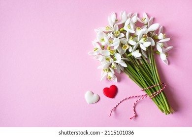 A bouquet of spring snowdrop flowers and red-white hearts on a pink background for the holiday of March 1, Valentine's Day.