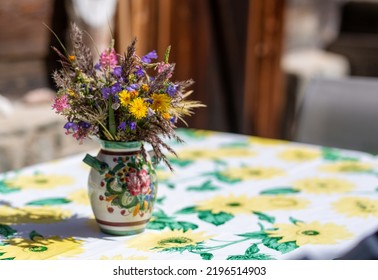 Bouquet Of Summer Wildflowers Village Style In A Vase On A Table With A Colourful Cover Outside With The Background Of Wooden Summer Cottage.