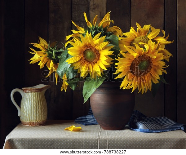 Bouquet of sunflowers in a\
clay jug on the table on the wooden background. Still life in\
rustic style.