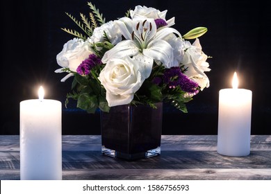 Bouquet of white flowers in a purple vase, white candle on a wooden boards. Vintage home decor dark tones. Condolence card or Valentines Card.