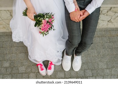 Bouquet of white and pink of roses in bride's hands. The bride and groom holding hands and wearing pink sneakers. Funny wedding couple. The newlywed together. Close up. Top view.