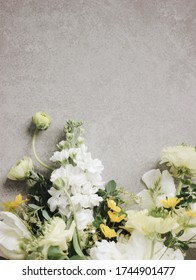 A Bouquet Of White And Yellow Spring Flowers (ranunculus/buttercup, Tulip, Peony, Matthiola, Spirea) Laying On The Gray Concrete Textured Background. High Angle View. Space For Copy.