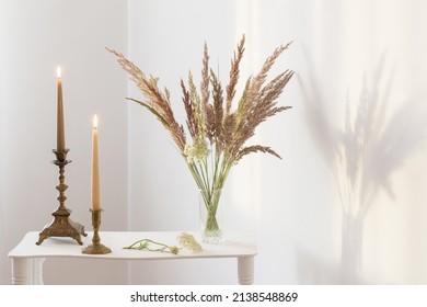 bouquet wild flowers and burning candles  in sunlight in white interior