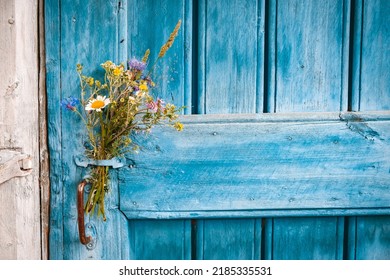 bouquet of wildflowers on the blue door of an old farmhouse. Rustic wooden planks background. Free space for text. minimal.
