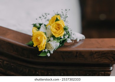 A bouquet of yellow roses and white flowers sits on a wooden surface. The arrangement is simple and elegant, with the yellow flowers providing a pop of color against the brown wood - Powered by Shutterstock