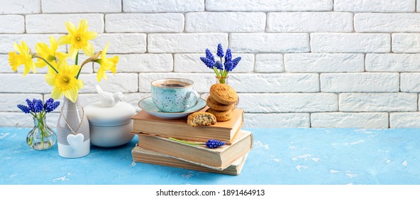 Bouquets Of Spring Flowers, Coffee Cup, Books, Cookies On Blue Table Over White Brick Background. Reading And Breakfast. Concept Spring, Hygge And Cozy Home Interior. Copy Space
