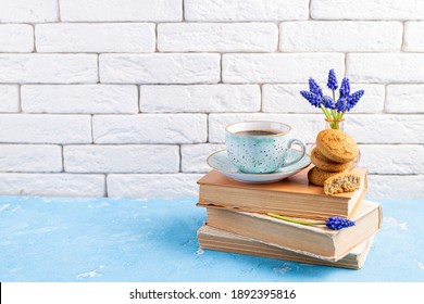 Bouquets Of Spring Flowers, Coffee Cup, Books, Cookies On Blue Table Over White Brick Background. Reading And Breakfast. Concept Spring, Hygge And Cozy Home Interior. Copy Space
