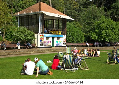 Bournemouth England. The Park In Which A Jazz Combo Are Playing On A Stage Covered With Red Tiled Roof Marquee With People Sitting Watching On The Grass And In Deck Chairs. Shrubs To Rear. 