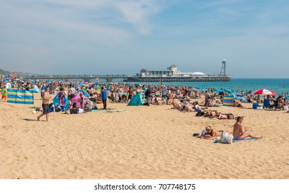 BOURNEMOUTH, UK - AUGUST 28, 2017: Busy beach in a hot summer day with Pier Amusements in the background