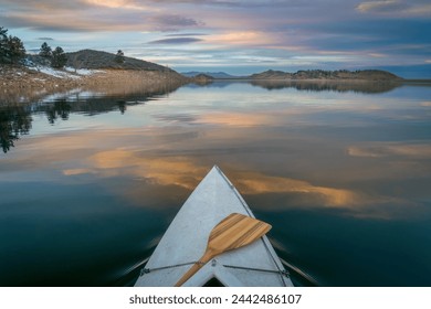 bow of expedition canoe with a wooden paddle at calm winter dusk over mountain lake - Horsetooth Reservoir - Powered by Shutterstock