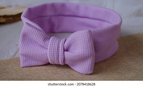 Bow headband made out of knit fabric with beautiful texture in soft purple color. A hair accessory with bow in front.
