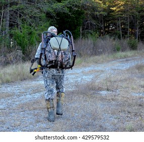 Bow Hunter Wearing Camouflage, Carrying Hunting Equipment Including Bow And Arrow And Tree Stand, Entering The Forest, Woods