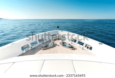 Bow of a new and modern Superyacht with teak deck, stainless steel capstans and cleats, with a nice view over blue sky and sea