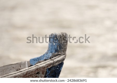 The bow of an old blue boat shows its textured history and character, set against the soft-focus backdrop of a rippling water surface