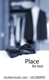 Bow Tie In Front Of Blurry Open Closet And Tuxedo With Isolated Place For Text. Blue Colorized Shot.