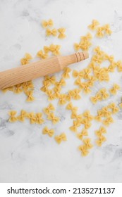 Bow tie pasta and rolling pin on light background. Top view. Flat lay.