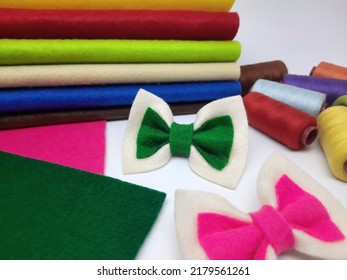 Bow tie ribbon crafts from flannel. Simple crafts for kids. Fibrous fabric texture. Selective focus on green ribbon with pile of colorful fabrics, threads and blurred background.