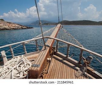 the bow of a traditional wooden boat with teak deck, hardwood bowsprit with blue sea and blue sky behind