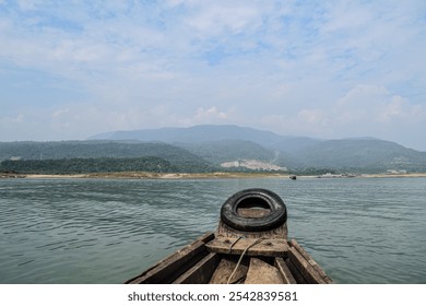 The bow of a wooden boat cuts through the tranquil waters of a river, offering a breathtaking view of green hills under a serene sky in the midday light. - Powered by Shutterstock