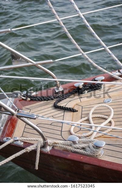 Bow of the yacht with mooring ropes.\
Wooden white deck with ropes on it and red hull. Yacht against the\
waves of the sea. A yacht with silver hand\
rails