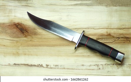 Bowie hunting knife on a wooden background. Combat army knife made of high- quality stainless steel. Weapons of attack and defense. The polished blade of the knife glitters.