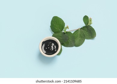 Bowl Of Activated Carbon Mask And Plant Branch On Color Background