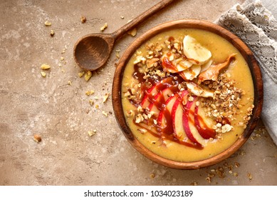 Bowl of apple banana smoothie with granola, caramel and peanut butter (apple pie) over beige or sand slate, stone or concrete background.Top view with copy space. - Powered by Shutterstock