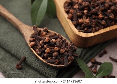 Bowl with aromatic cloves, spoon and green leaves on table, closeup