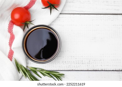 Bowl with balsamic vinegar, rosemary and tomatoes on white wooden table, flat lay. Space for text