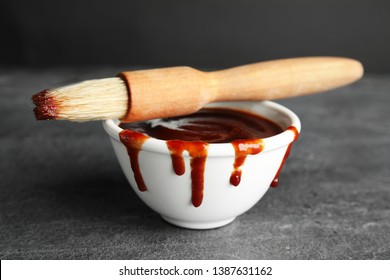 Bowl With Barbecue Sauce And Brush On Grey Table