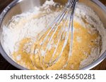 Bowl of batter and whisk on wooden table. Close-up of mixing dough for bakery and cooking. Ingredients for waffles, cakes or pancakes. Dough preparation process