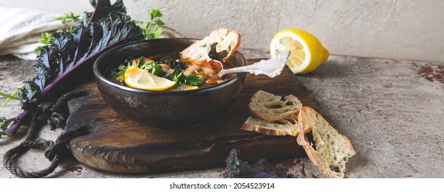 A Bowl Of Bean Soup With Kale And Lemon On The Table