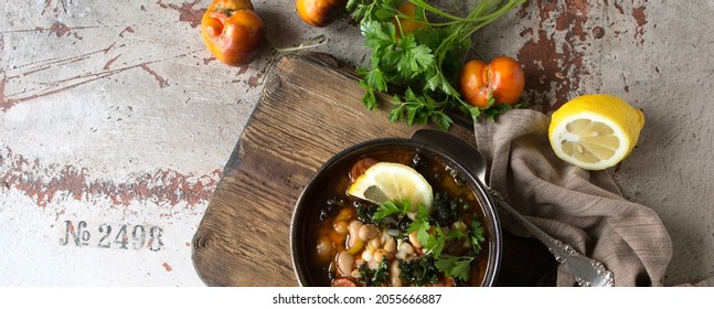 A Bowl Of Bean Soup With Kale And Lemon On The Table