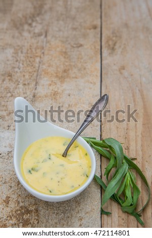 Bowl with bearnaise sauce, tarragon and a spoon on an old wooden background