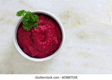 Bowl of beet hummus dip, above view on a white marble background