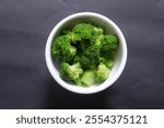 A bowl of blanched broccoli placed in a dark background