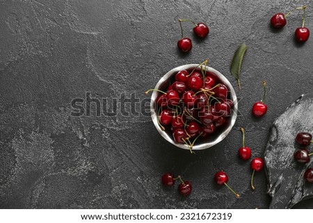 Bowl and board with sweet cherries on black background