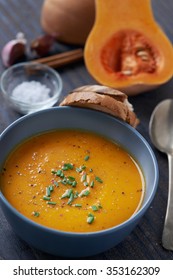 Bowl Of Butternut Soup Garnished With Chives, Raw Ingredients In The Background