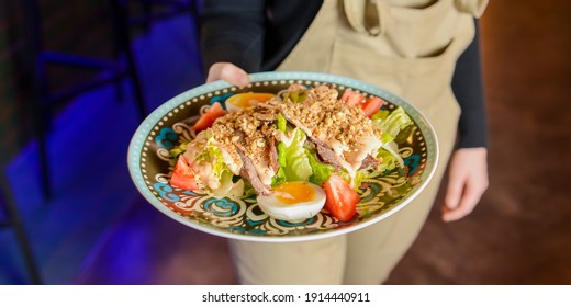 Bowl Of Caesar Salad Served In A Blue Bowl By Waiter In Resturant Or Diner. Healthy Dinner, Traditional Recipe. Copy Space Banner.