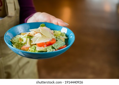 Bowl Of Caesar Salad Served In A Blue Bowl By Waiter In Resturant Or Diner. Healthy Dinner, Traditional Recipe. Copy Space Banner.