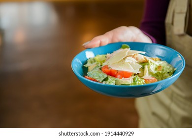 Bowl Of Caesar Salad Served In A Blue Bowl By Waiter In Resturant Or Diner. Healthy Dinner, Traditional Recipe. Copy Space Banner.