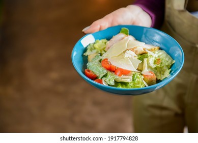 Bowl Of Caesar Salad Served In A Blue Bowl By Waiter In Resturant Or Diner. Healthy Dinner, Traditional Recipe. Copy Space Banner.