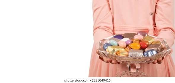 Bowl of candies,  child holding bowl of candies. Isolated white background, copy space. Offering luxury chocolate and almond dragee. Sugar feast banner concept idea. Delicious assorted sweets.