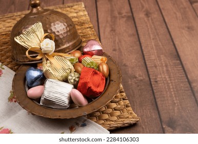 Bowl of candies, close up image of antique copper bowl of candies. Wrapped chocolate and almond dragee  on the wooden table. Copy space. Many colorful treats. Text area for ramadan feast greeting.