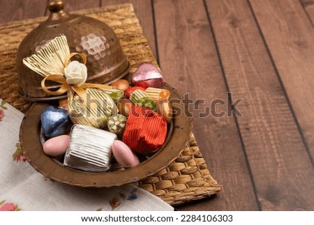 Bowl of candies, close up image of antique copper bowl of candies. Wrapped chocolate and almond dragee  on the wooden table. Copy space. Many colorful treats. Text area for ramadan feast greeting.