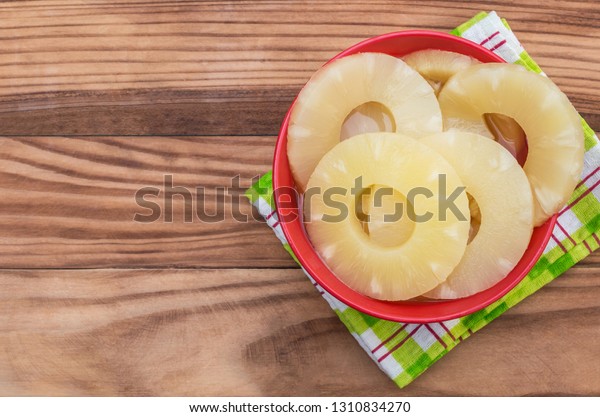 Bowl with canned pineapple rings on wooden table.\
Top view. Space for text.