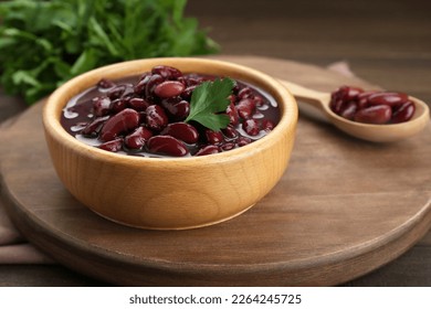Bowl of canned red kidney beans with parsley on wooden table, closeup